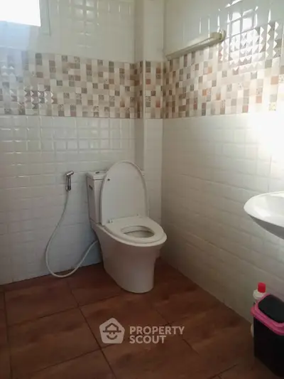 Modern bathroom with tiled walls and floor, featuring a sleek toilet and bidet spray.