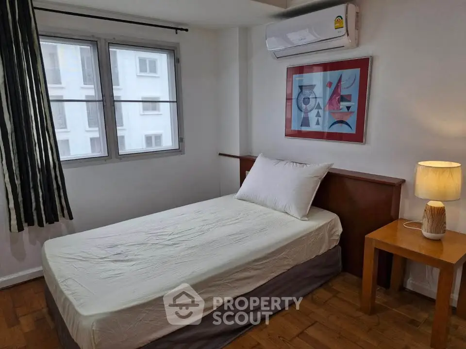 Cozy bedroom with single bed, modern art, and natural light from large windows.