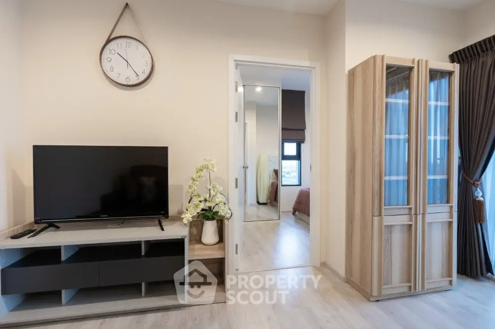 Modern living room with TV, wooden cabinet, and view into bedroom, showcasing stylish interior design.