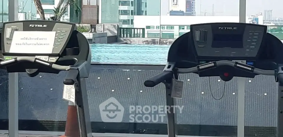 Modern gym with treadmills overlooking a stunning rooftop pool and city view.