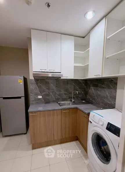 Modern kitchen with sleek cabinets, washing machine, and stainless steel fridge in a compact layout.
