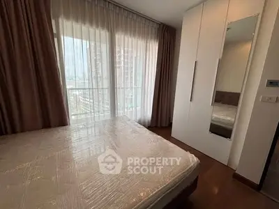 Modern bedroom with large window and built-in wardrobe in high-rise apartment.