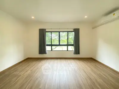 Spacious empty room with large window and wooden flooring, perfect for customization.