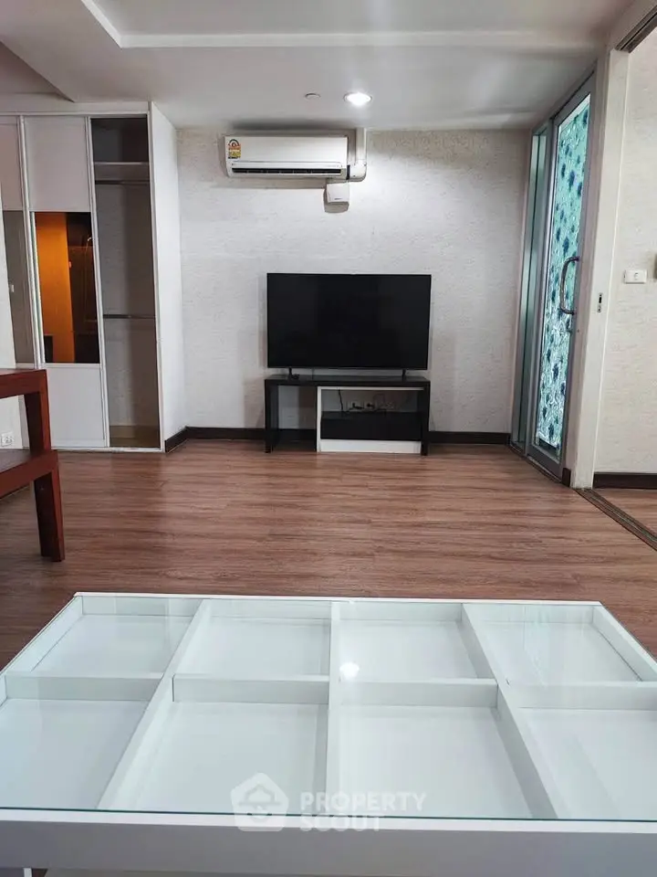 Modern living room with sleek furniture and wooden flooring, featuring a flat-screen TV and air conditioning.