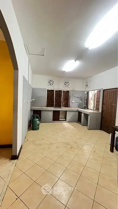 Spacious kitchen with tiled floor and ample natural light, featuring a closed layout and wooden cabinetry.