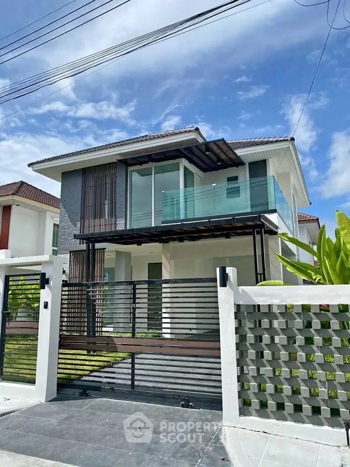 Modern two-story house with glass balcony and stylish facade under a clear blue sky.