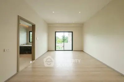 Spacious empty room with wooden flooring and large window offering natural light and greenery view.