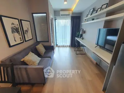 Modern living room with stylish decor, large TV, and natural light from balcony.