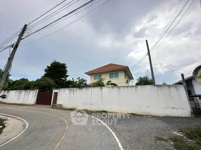 Charming suburban house with red roof and white walls, nestled behind a tall fence on a quiet curved street.