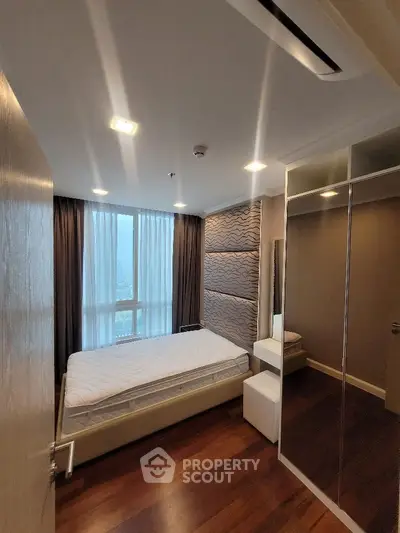 Modern bedroom with large window and mirrored closet in high-rise apartment.