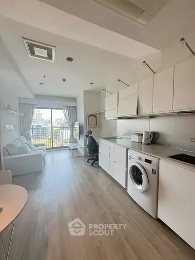 Modern studio apartment with open kitchen and city view balcony, featuring sleek white cabinetry and in-unit washer.
