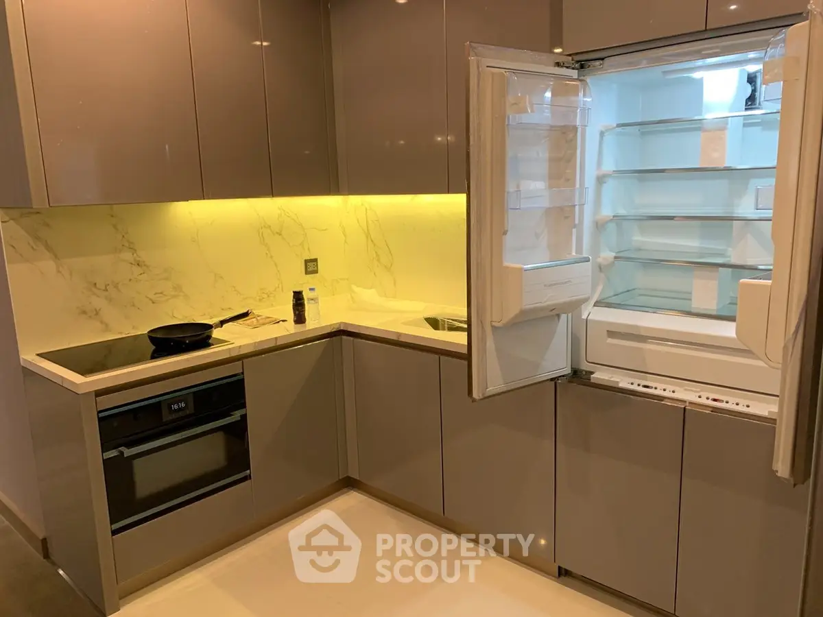 Modern kitchen with sleek cabinetry, built-in oven, and open fridge showcasing spacious interior.