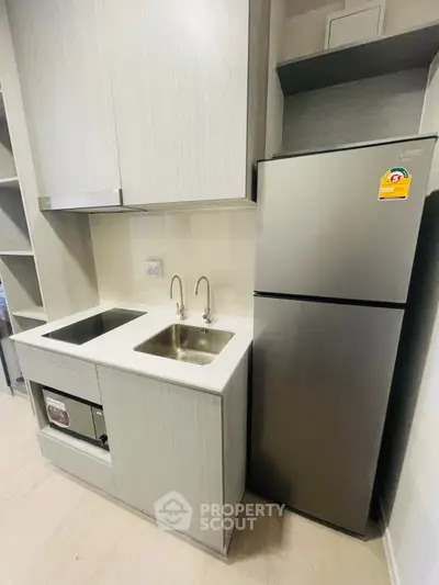 Modern compact kitchen with sleek appliances and minimalist design, featuring a stainless steel fridge and dual sink.