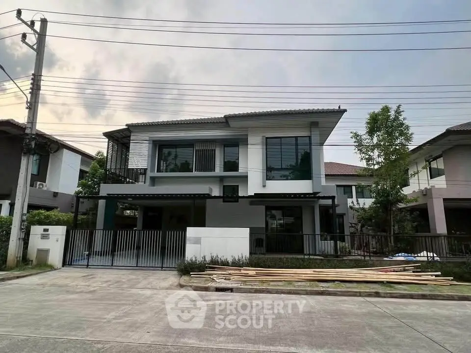 Modern two-story house with large windows and gated driveway in a suburban neighborhood.