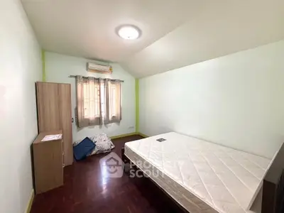 Spacious bedroom with wooden flooring and natural light, featuring a minimalist design and air conditioning.