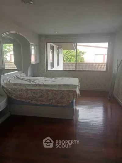 Cozy bedroom with floral decor and large window offering natural light and serene views.