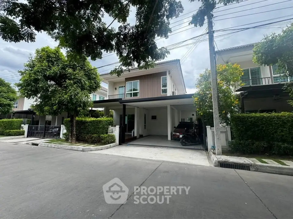 Modern two-story house with carport and lush greenery in a serene neighborhood.