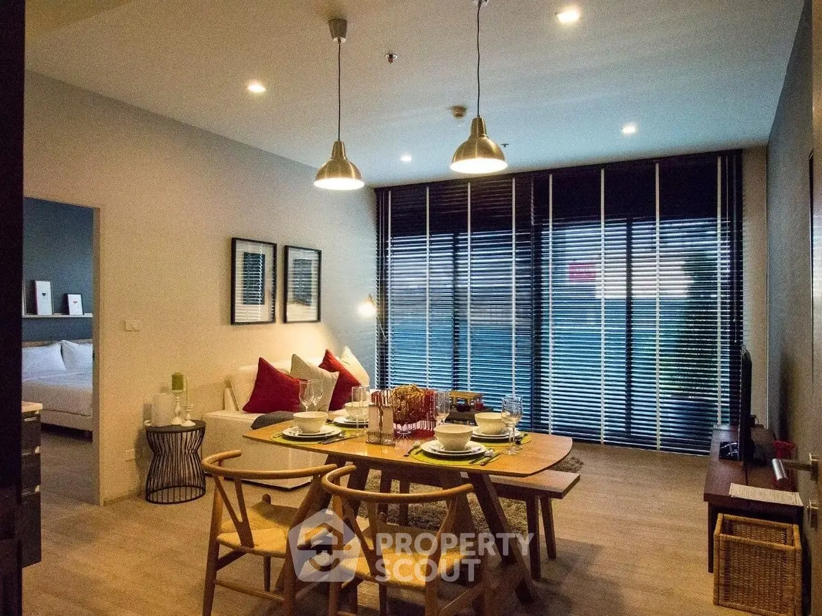 Modern living room with dining area, stylish furniture, and large windows with blinds.