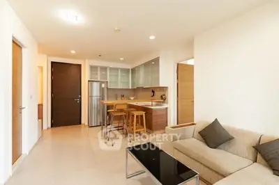 Modern open-layout living room with kitchen, featuring sleek furniture and neutral tones.