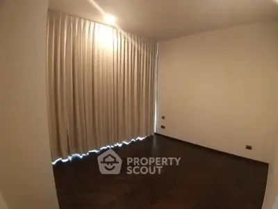 Spacious empty room with elegant dark wood flooring and floor-to-ceiling curtains.