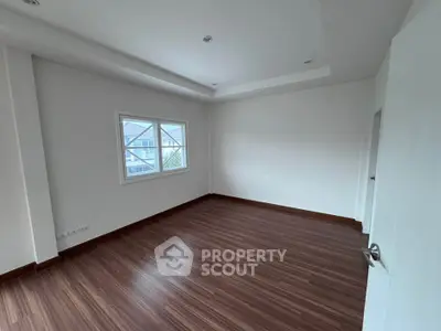 Spacious empty room with wooden flooring and large window, perfect for customization.