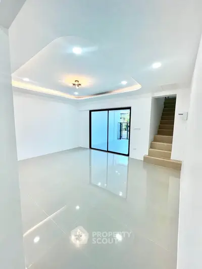 Spacious modern living room with sleek tile flooring and recessed lighting, featuring a staircase and large sliding doors.