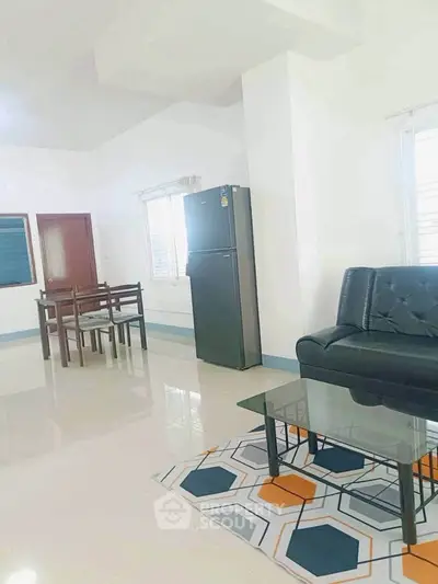 Spacious living room with modern furniture and dining area, featuring a sleek refrigerator and stylish decor.