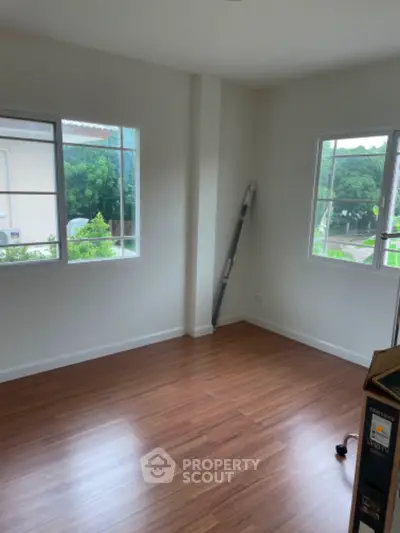 Spacious empty room with wooden flooring and large windows offering natural light.