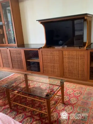 Cozy living room interior featuring a vintage wooden entertainment center with a modern flat-screen TV and a classic glass-top coffee table on an ornate rug.