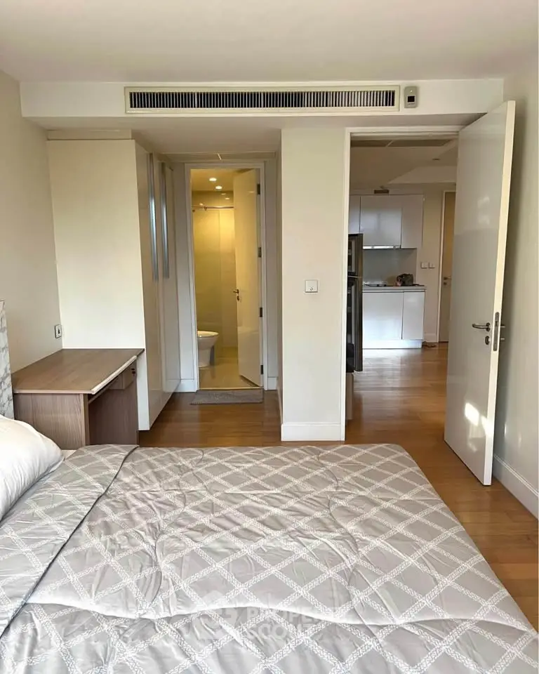 Modern bedroom with ensuite bathroom and view into kitchen area, featuring sleek design and wooden flooring.