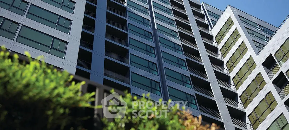 Modern high-rise apartment building with sleek glass facade and lush greenery.