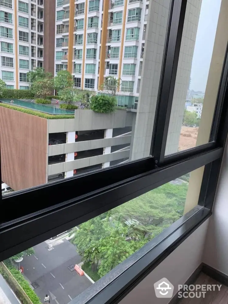 Modern high-rise building view from window with lush greenery and urban landscape.