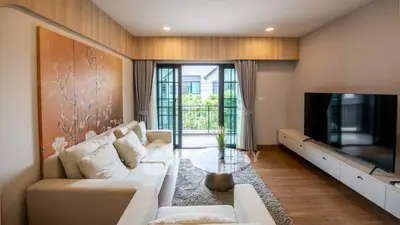 Modern living room with large TV and balcony view, featuring elegant decor and natural light.