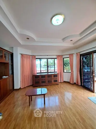 Spacious living room with wooden flooring and large windows offering natural light.