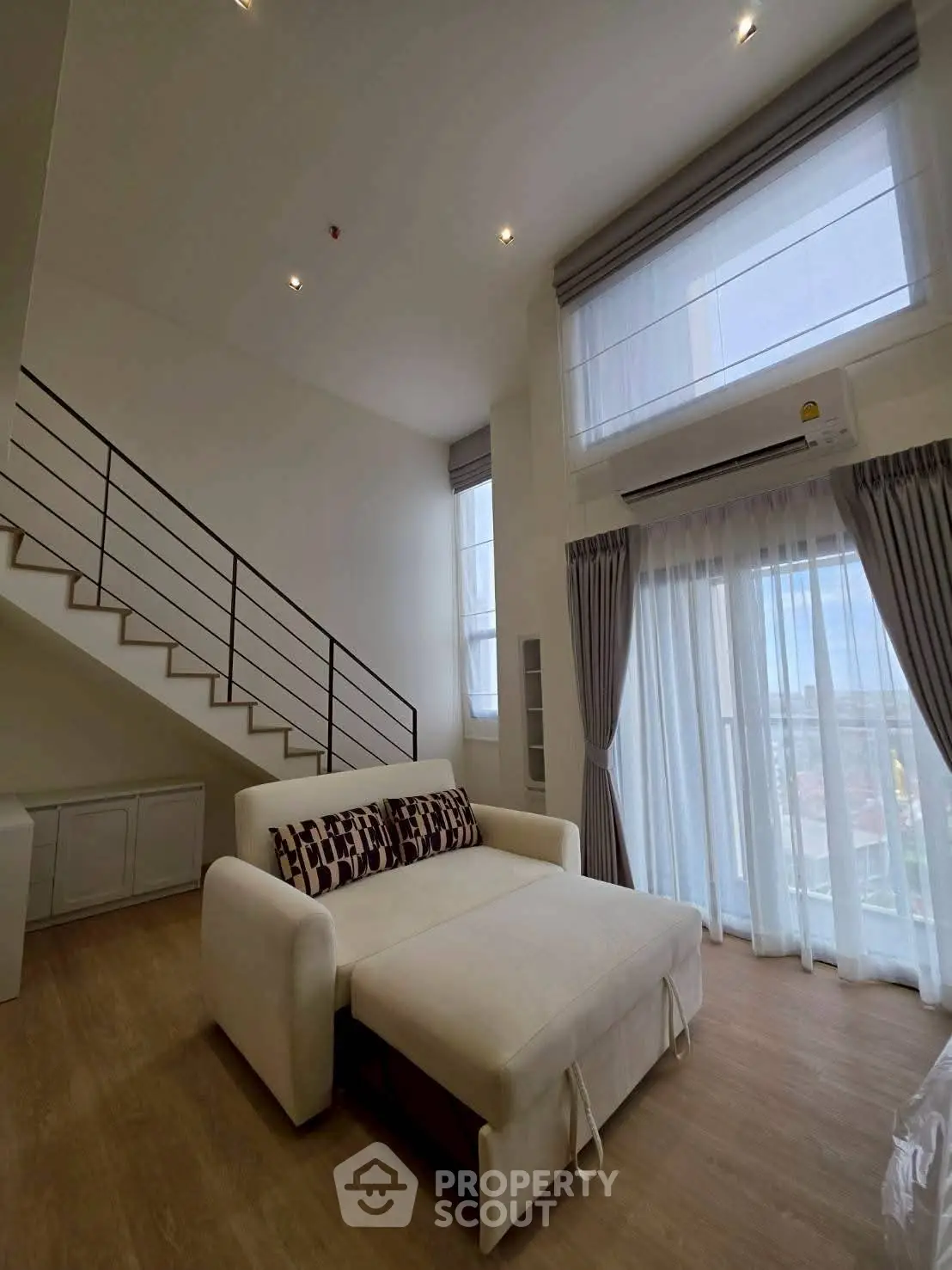 Spacious modern living room with high ceilings and large windows offering natural light and city views.