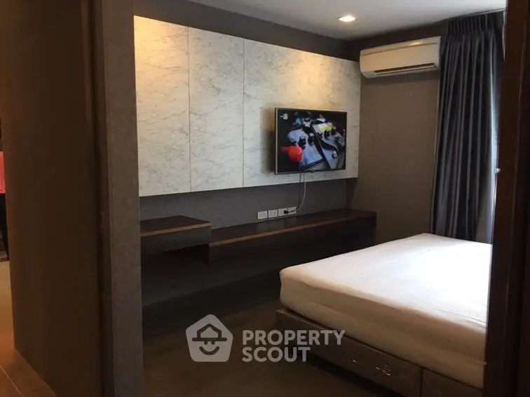 Modern bedroom with wall-mounted TV and air conditioning in stylish apartment.