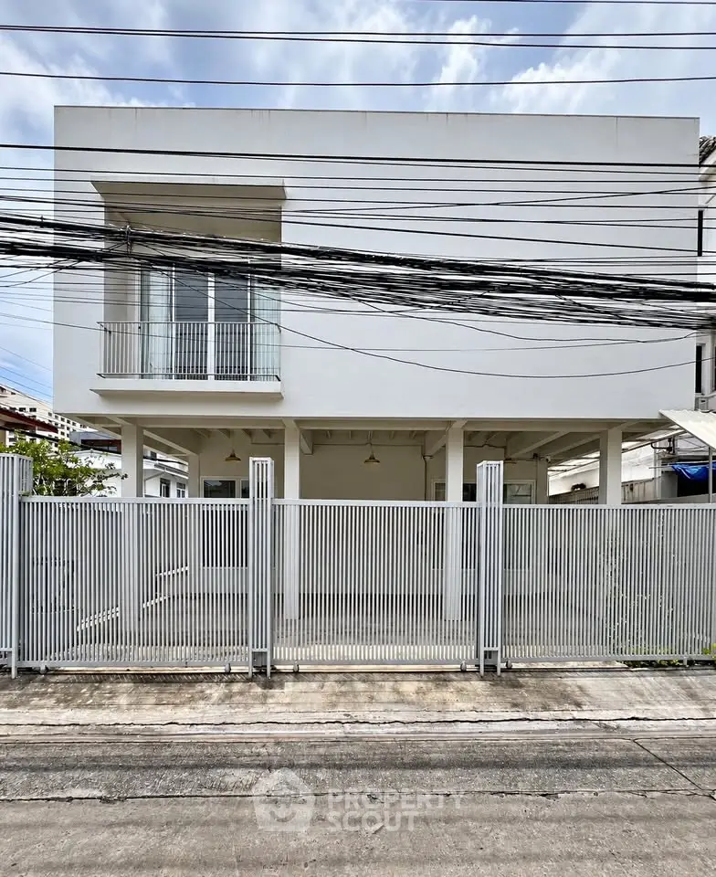 Modern minimalist white building exterior with gated entrance and clear sky backdrop.