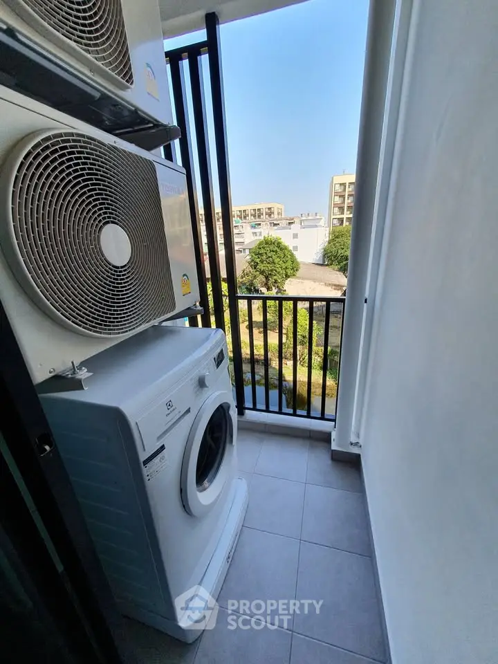 Compact balcony with washing machine and air conditioning units, offering a city view.