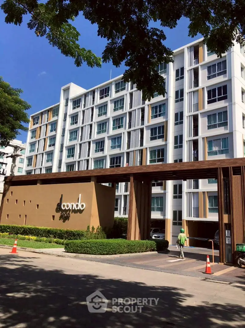 Modern condo building exterior with lush landscaping and clear blue sky.
