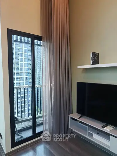 Modern living room with floor-to-ceiling windows and city view, featuring sleek TV setup and elegant curtains.