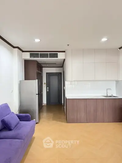 Modern open-layout kitchen with sleek cabinetry and cozy living area featuring a purple sofa.