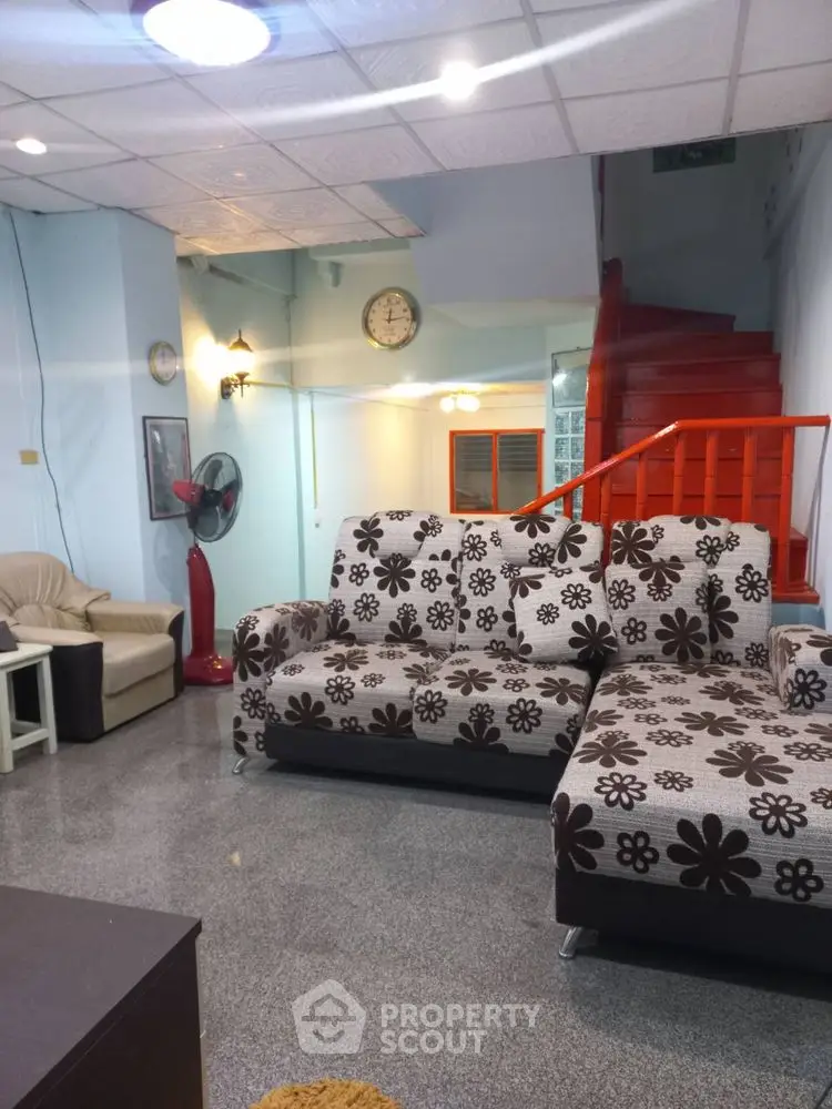 Spacious living room with floral sofas and red staircase