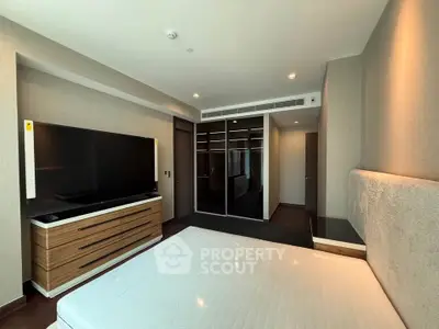 Spacious modern bedroom with large TV and mirrored wardrobe in luxury apartment.