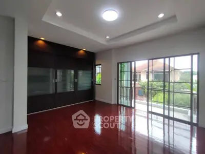 Spacious living room with hardwood floors and large windows overlooking greenery.