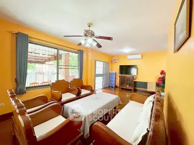Spacious living room with wooden furniture and bright orange walls, featuring a ceiling fan and large window.