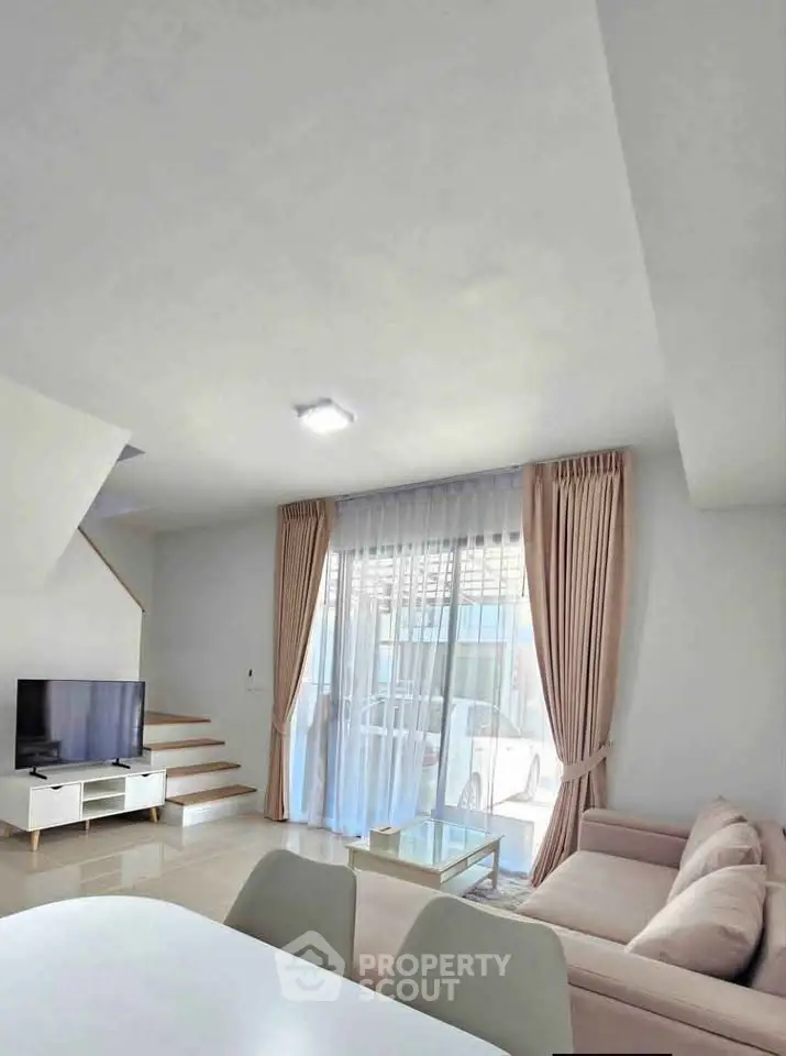 Modern living room with large windows, cozy sofa, and sleek TV setup in a bright, airy space.