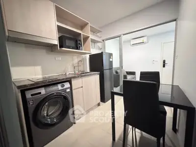 Modern kitchen with washing machine, microwave, and dining area in compact apartment.