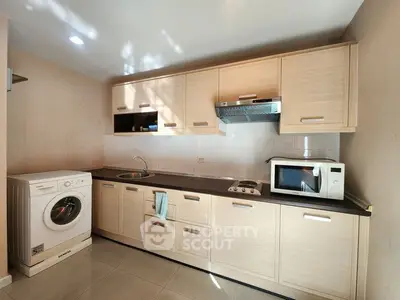 Modern kitchen with wooden cabinets, washing machine, and microwave, perfect for urban living.