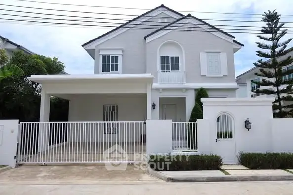 Charming two-story white house with gated driveway and lush greenery