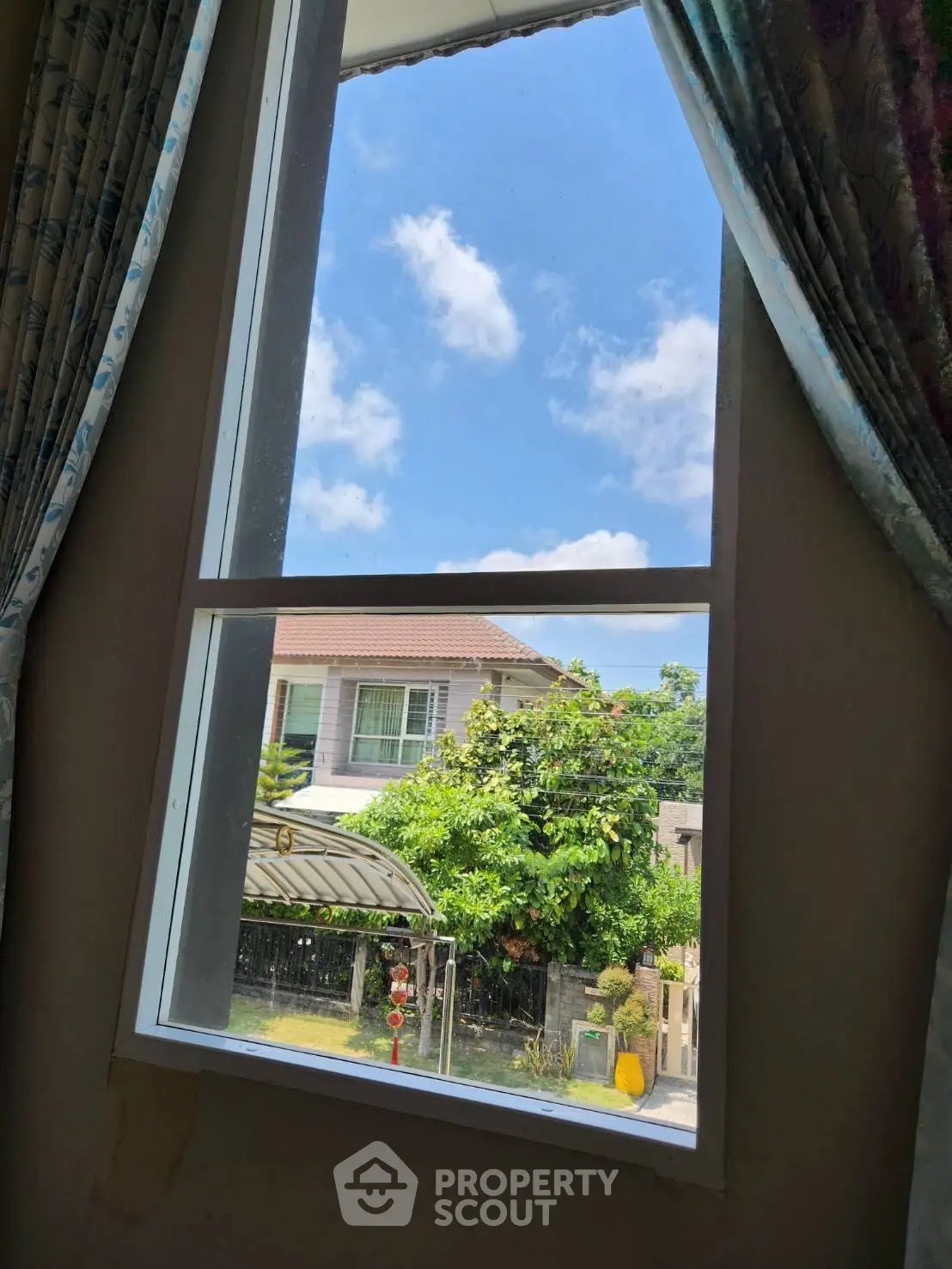 Charming view from a window showcasing a suburban house and lush greenery under a clear blue sky.